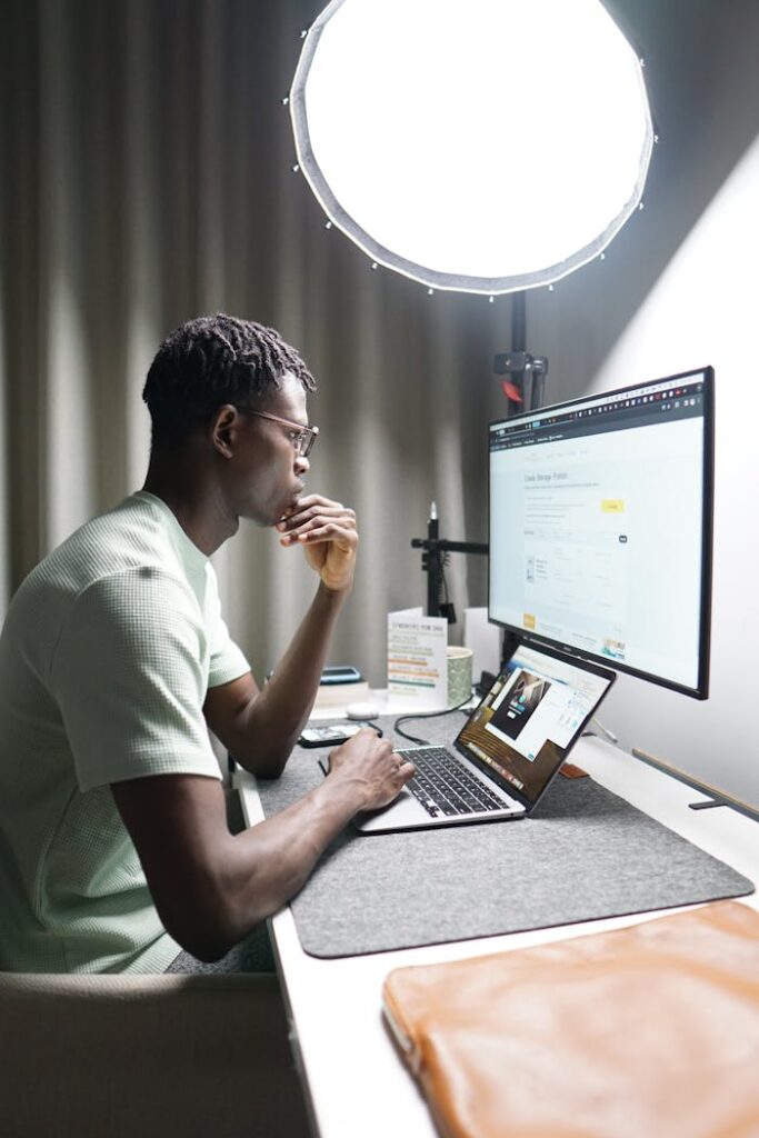Young man working remotely on laptop and monitor with bright studio lighting.